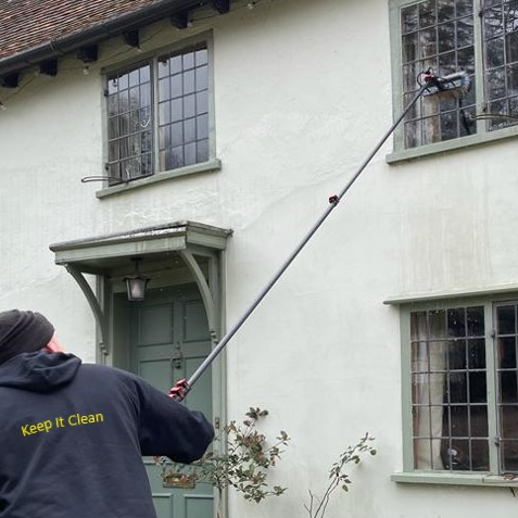 A man using a pole to clean a window from outside a two-storey house.