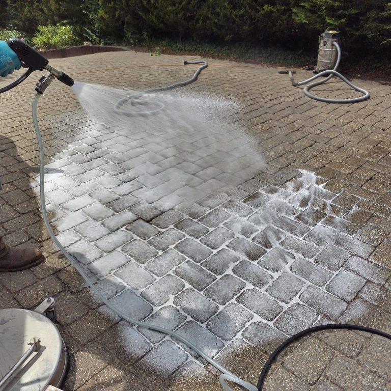 A person using a pressure washer to clean a patio surface.