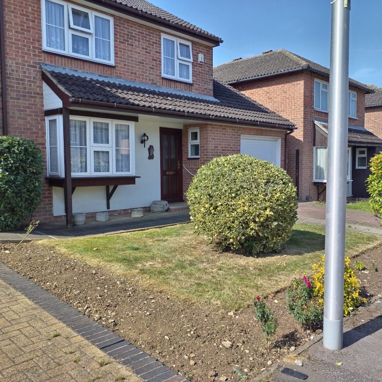 Two-storey brick house with a front garden and a large bush, alongside a paved driveway.